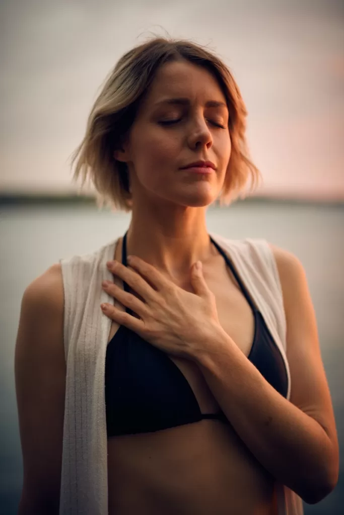 woman in white vest and black bikini with hand on chest. zen relaxation