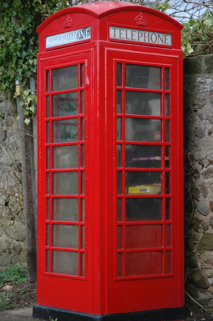 red wooden telephone booth beside gray concrete stonewall at daytime